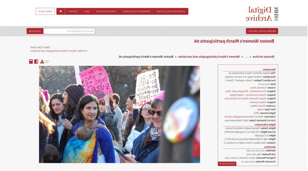 Screenshot from the MHS Digital Archive showing Boston Women’s March participants image 06.  A column of metadata is on the left.  The image depicts a large crowd of people standing close to each other, two people are holding signs.  A woman on the left appears to be looking at her cell phone. A woman in the middle of the photograph is looking to the left at various people and she is carrying an infant in a colorful tie-dye sling.  